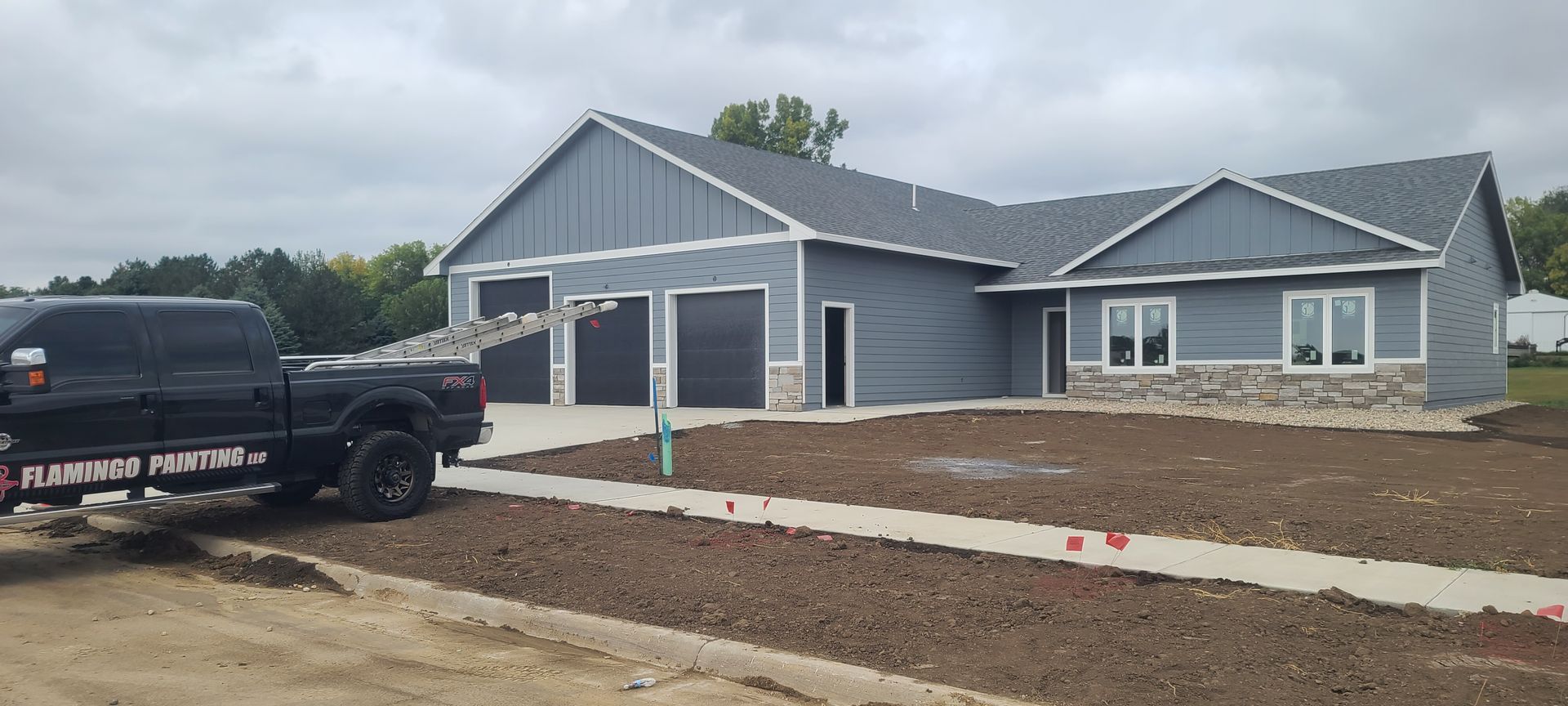 A new house with a three-car garage and a black truck parked in front. Gray siding and a cloudy sky.