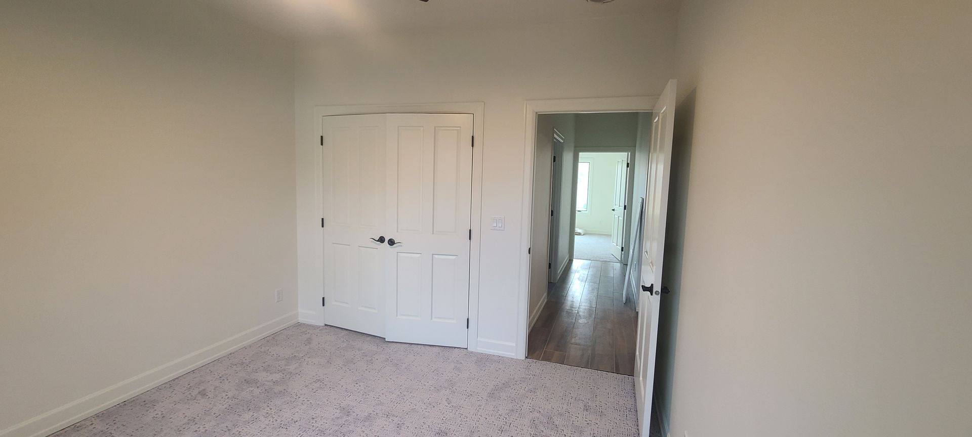 A nearly empty room with a closed closet and an open doorway to a hallway, both with white trim.