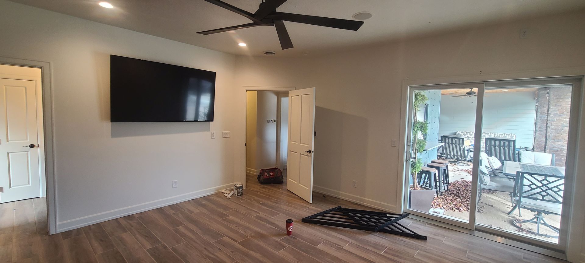 A room with a TV mounted on the wall, a sliding glass door to a patio, and a ceiling fan.