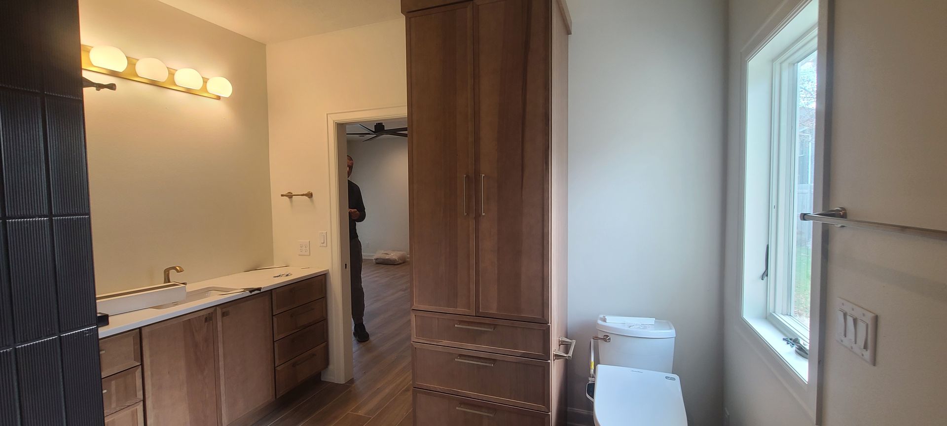 A bathroom with wooden cabinets, a toilet, a window, and a tall cabinet.