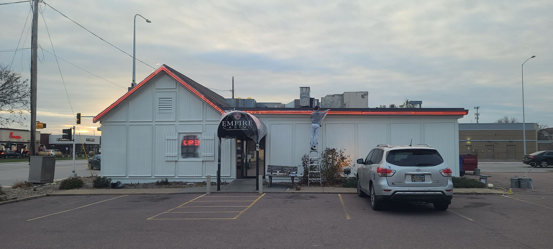White restaurant with red trim, black entrance awning, and car parked in front.