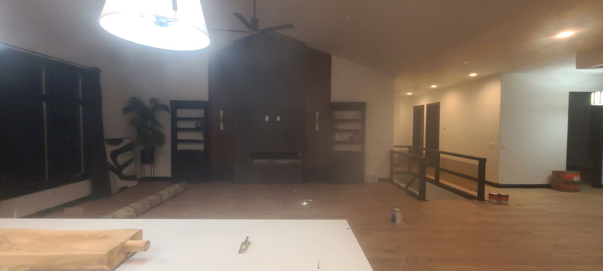 An empty room with a dark wooden wall feature. There are built-in shelves on either side, a ceiling fan, and a light fixture.