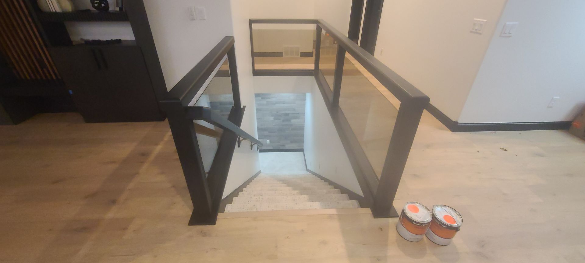 Staircase with glass and metal railings leads down to a lower level. Paint buckets sit at the base of the stairs.