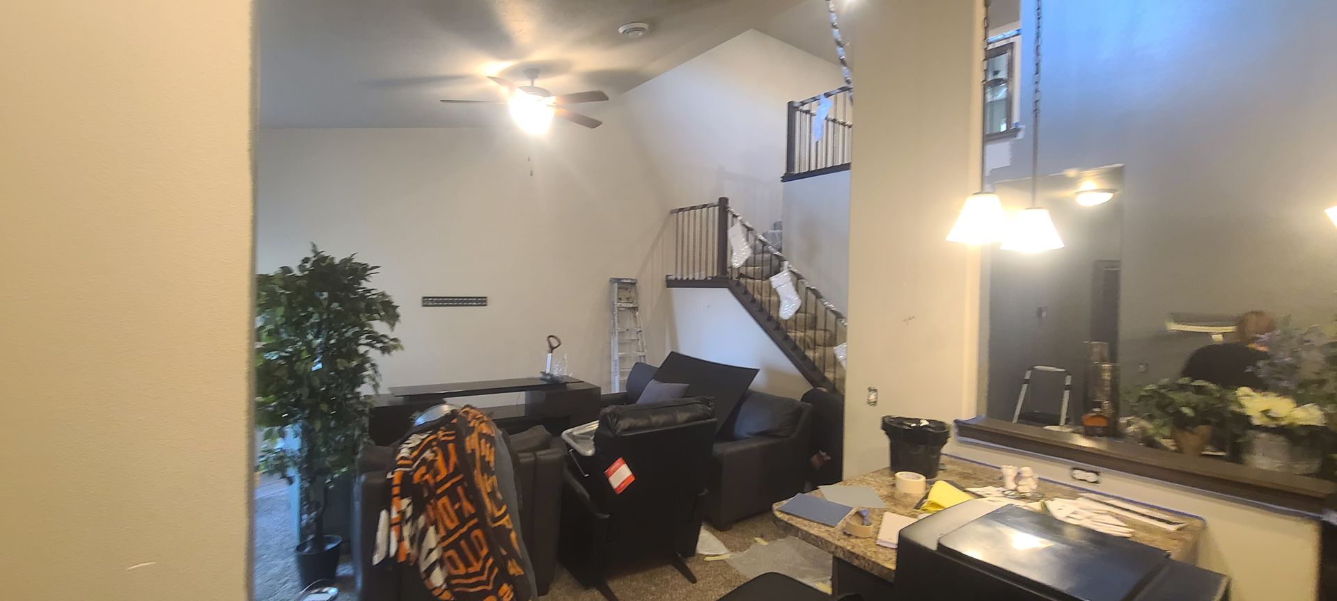 Living room with a sofa, stairs, and a large plant. A light fixture and ceiling fan are also visible.