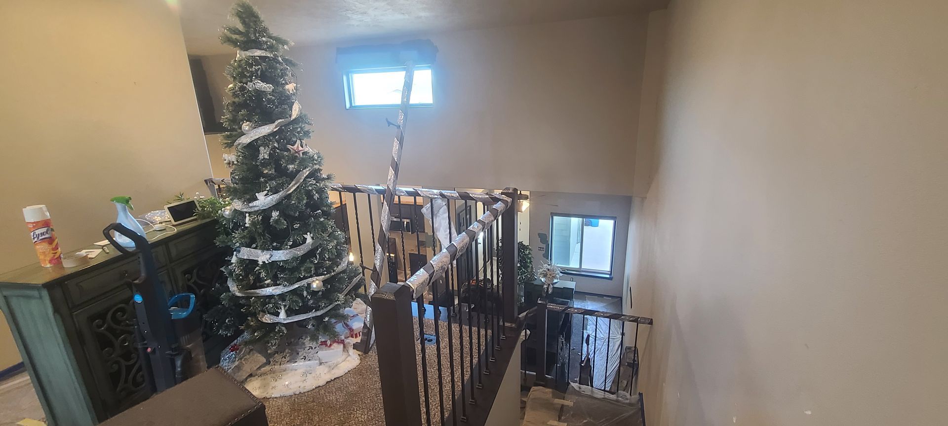 A Christmas tree decorated with white garland sits near a staircase. The staircase leads down to a lower level.