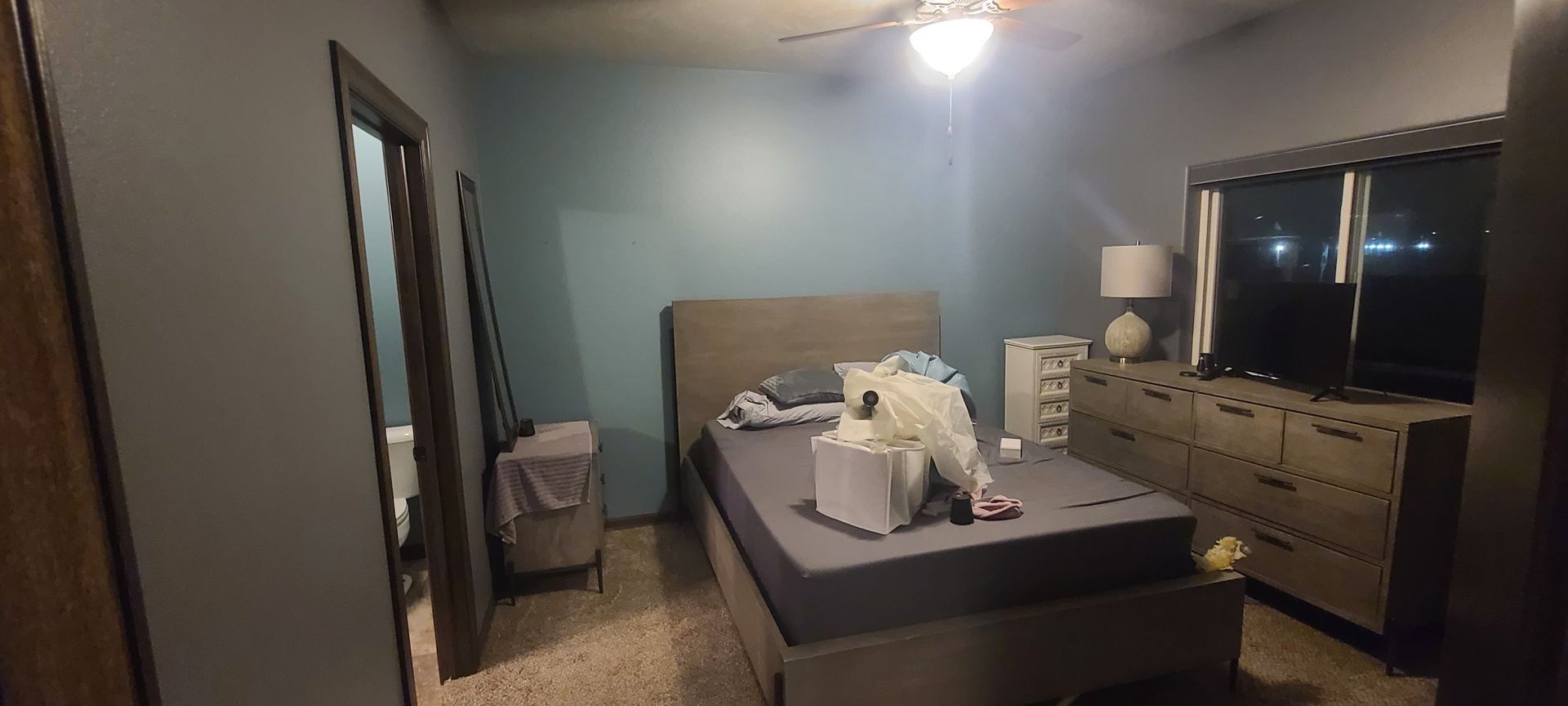 A bedroom with a bed, dresser, and a door open to the bathroom. The walls are blue.