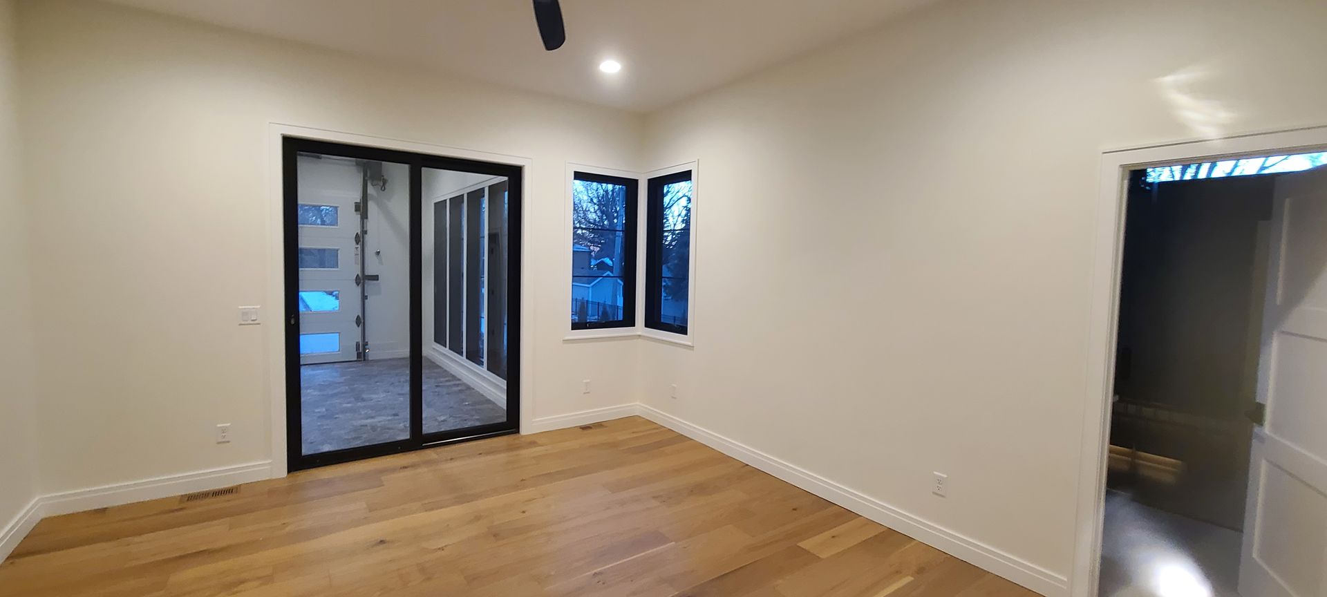 Empty room with wooden floor, black-framed doors, and windows, cream-colored walls, and a door on the right.