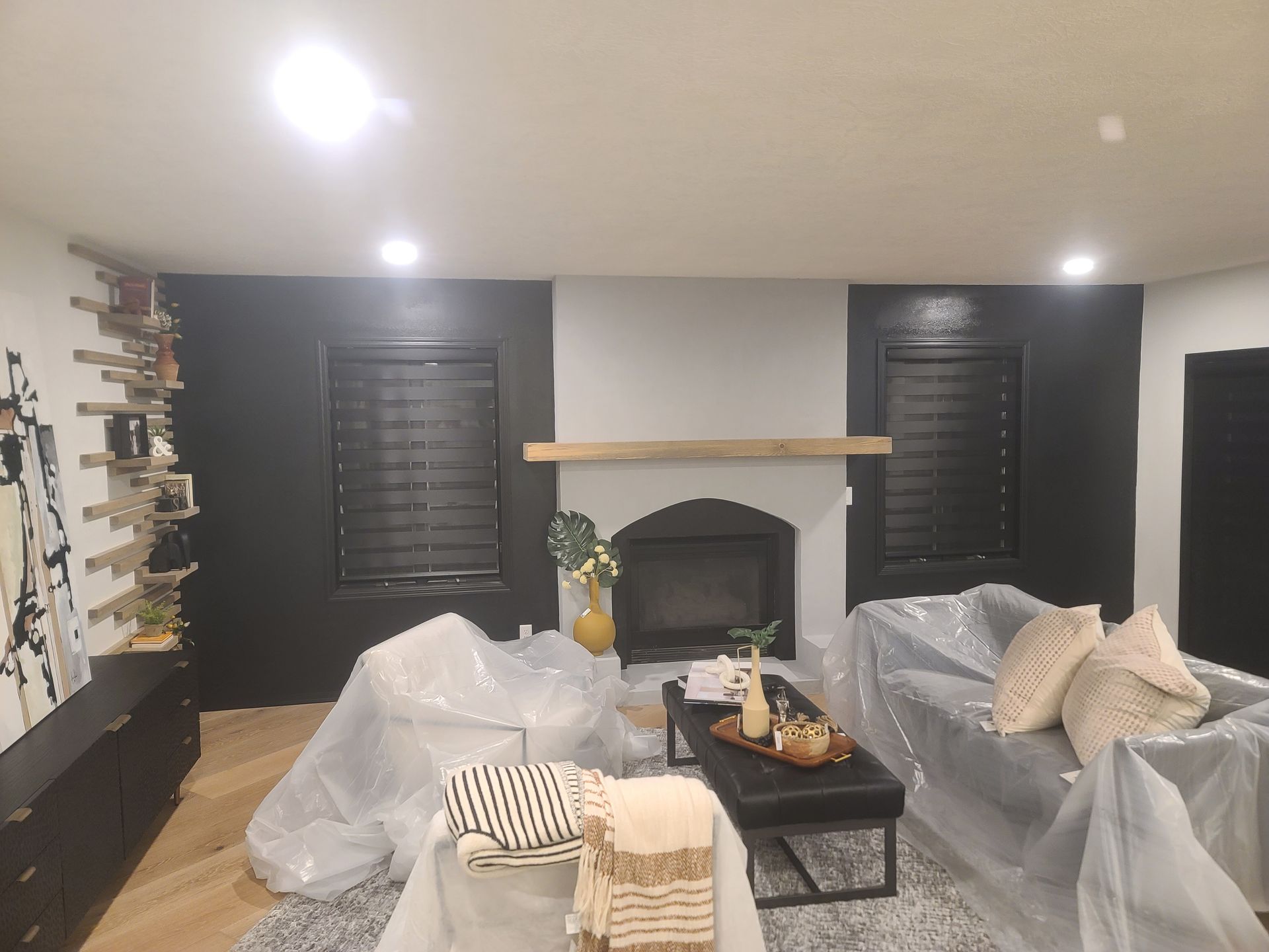 Living room with black accent walls, fireplace, covered furniture, and wooden shelf.