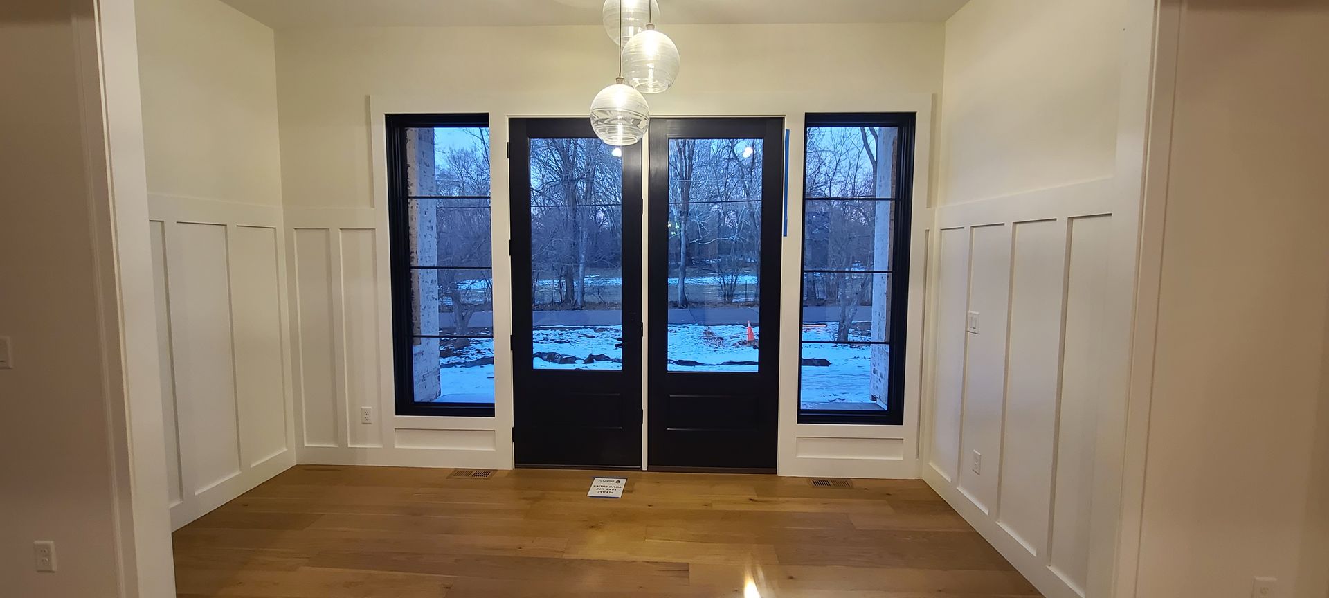 A room with black framed doors and windows, light walls, and wood floor. A chandelier hangs from the ceiling.