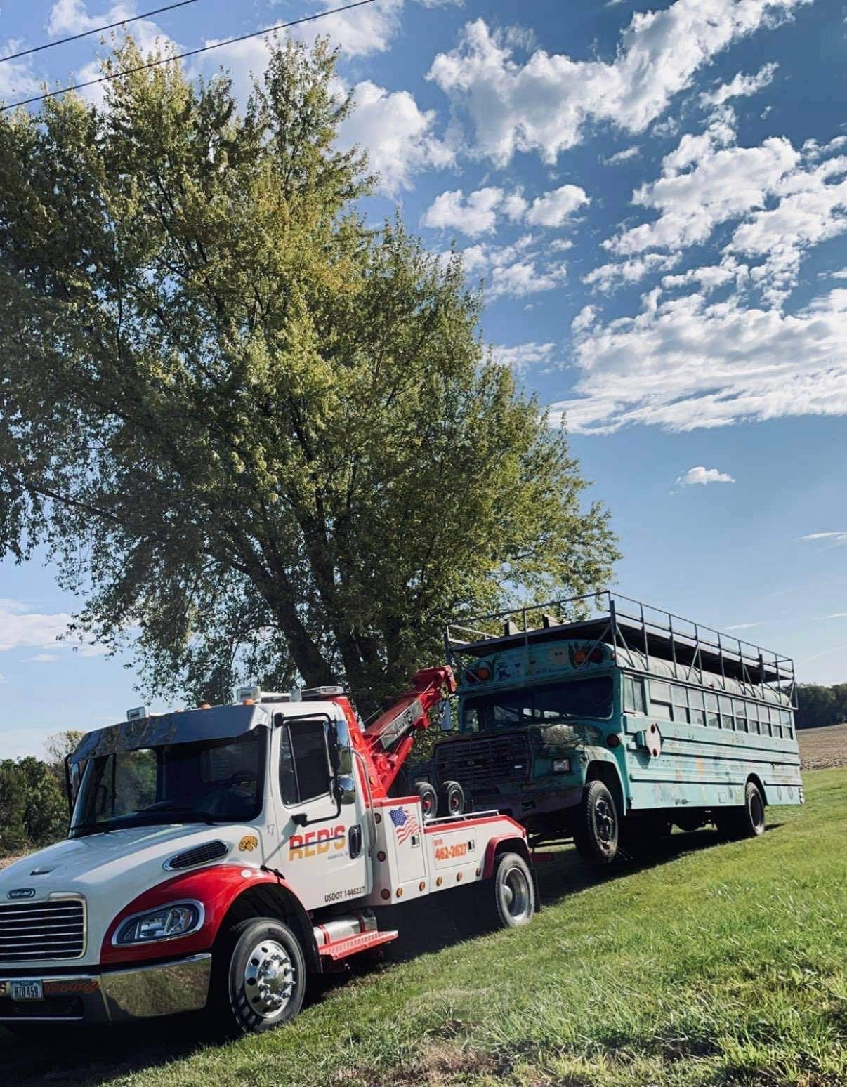 A tow truck is towing a school bus in a field.