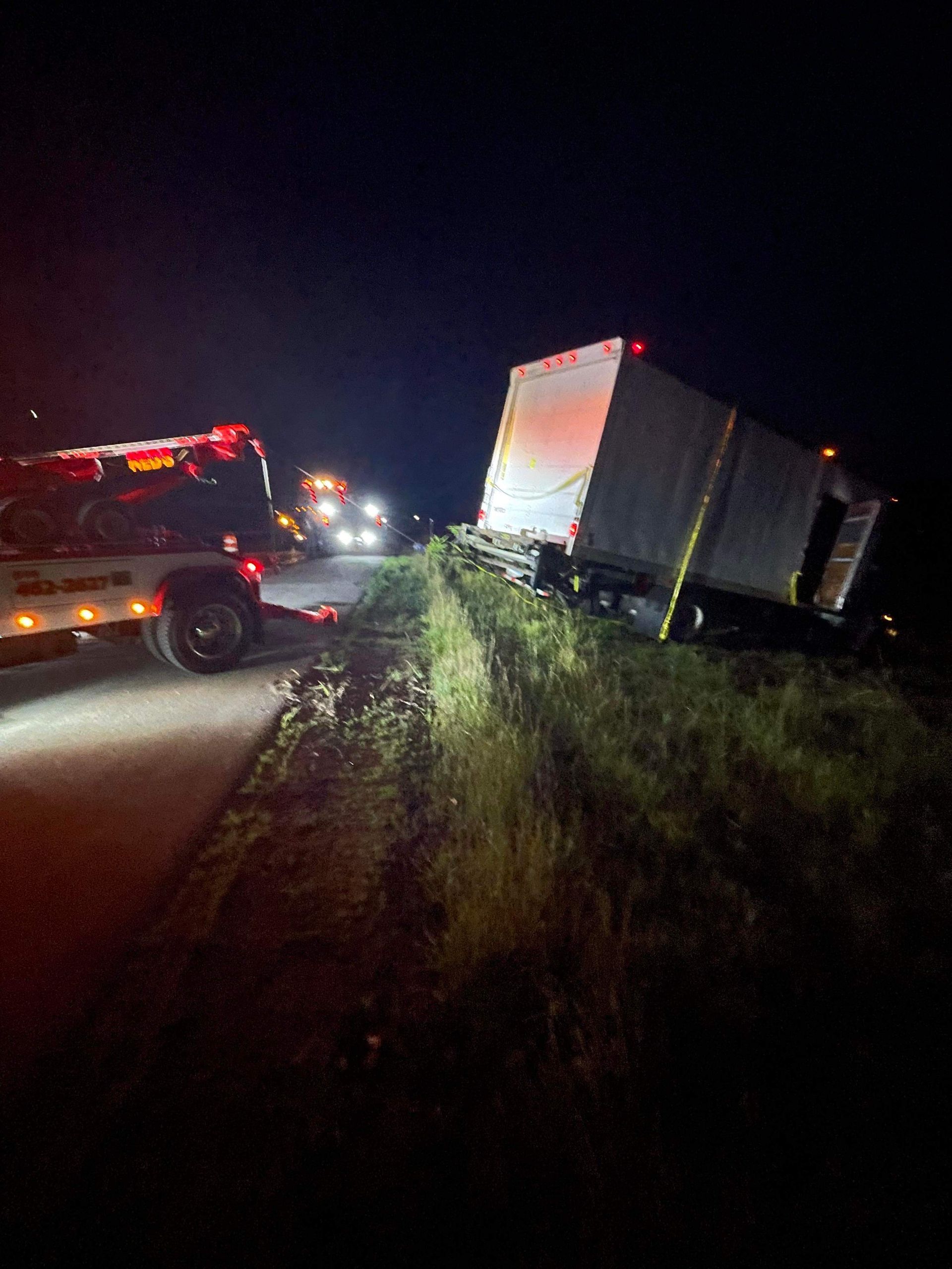 A tow truck is towing a semi truck that has fallen off the road at night.