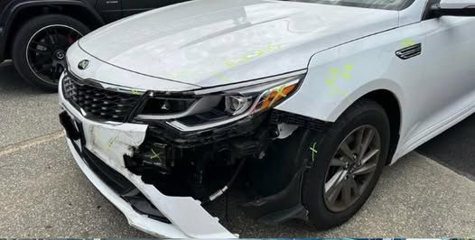 A silver car with a large dent on the side panel.