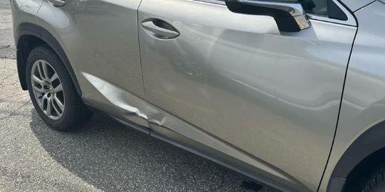 A silver car with a large dent on the side panel.