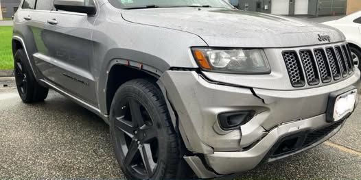Silver Jeep Grand Cherokee with black wheels and front bumper damage.