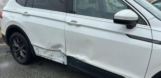 White SUV with significant damage to the side panel, including dents and exposed metal.