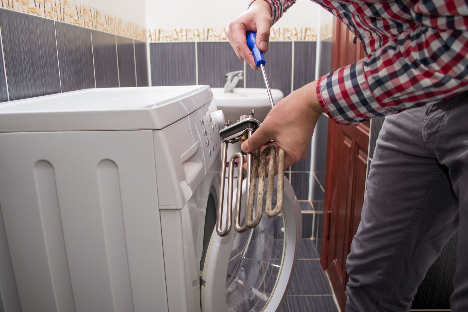 Person repairing a washing machine with tools beside a tiled wall