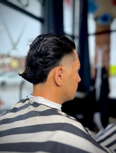 Man with dark, wavy hair, fade haircut, wearing striped barber cape.