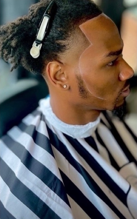 Person with a geometric hairline design, wearing a barber's cape, and hair clip.