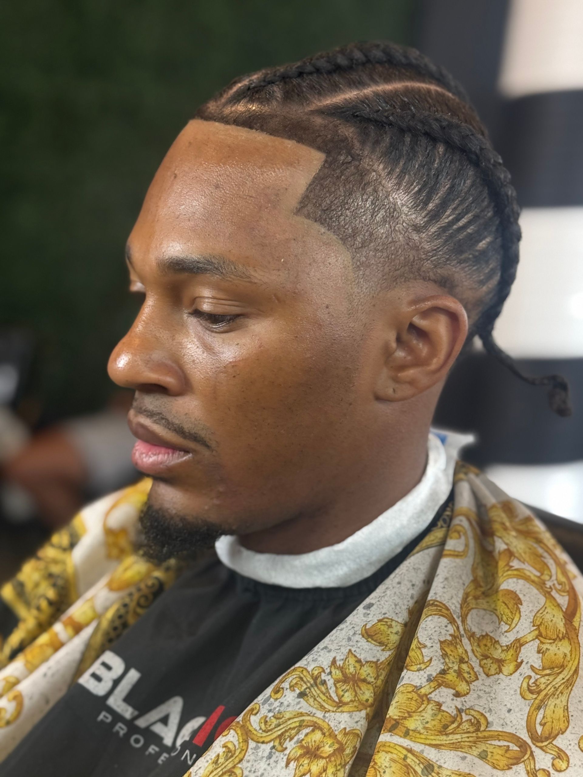 Man with braided hair and a neatly trimmed hairline. He wears a cape with gold designs.