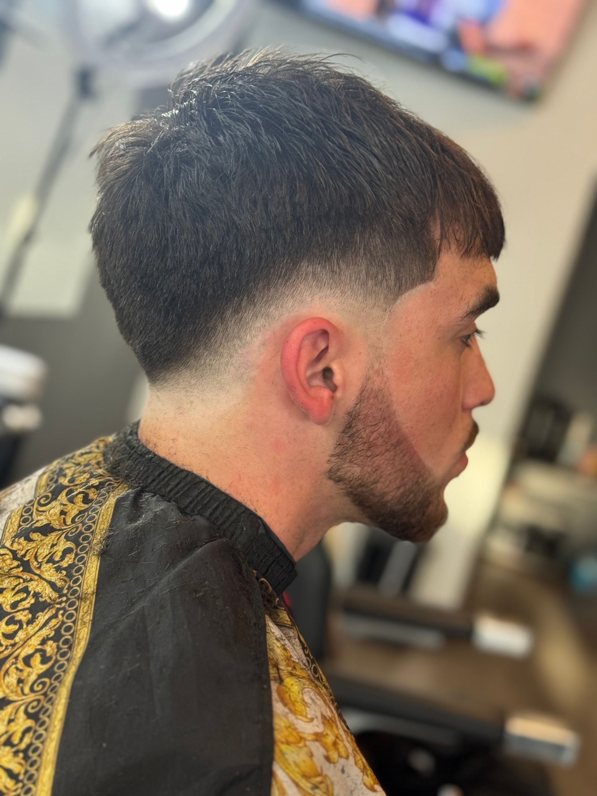 Man with faded haircut and beard in a barber's cape, profile view.