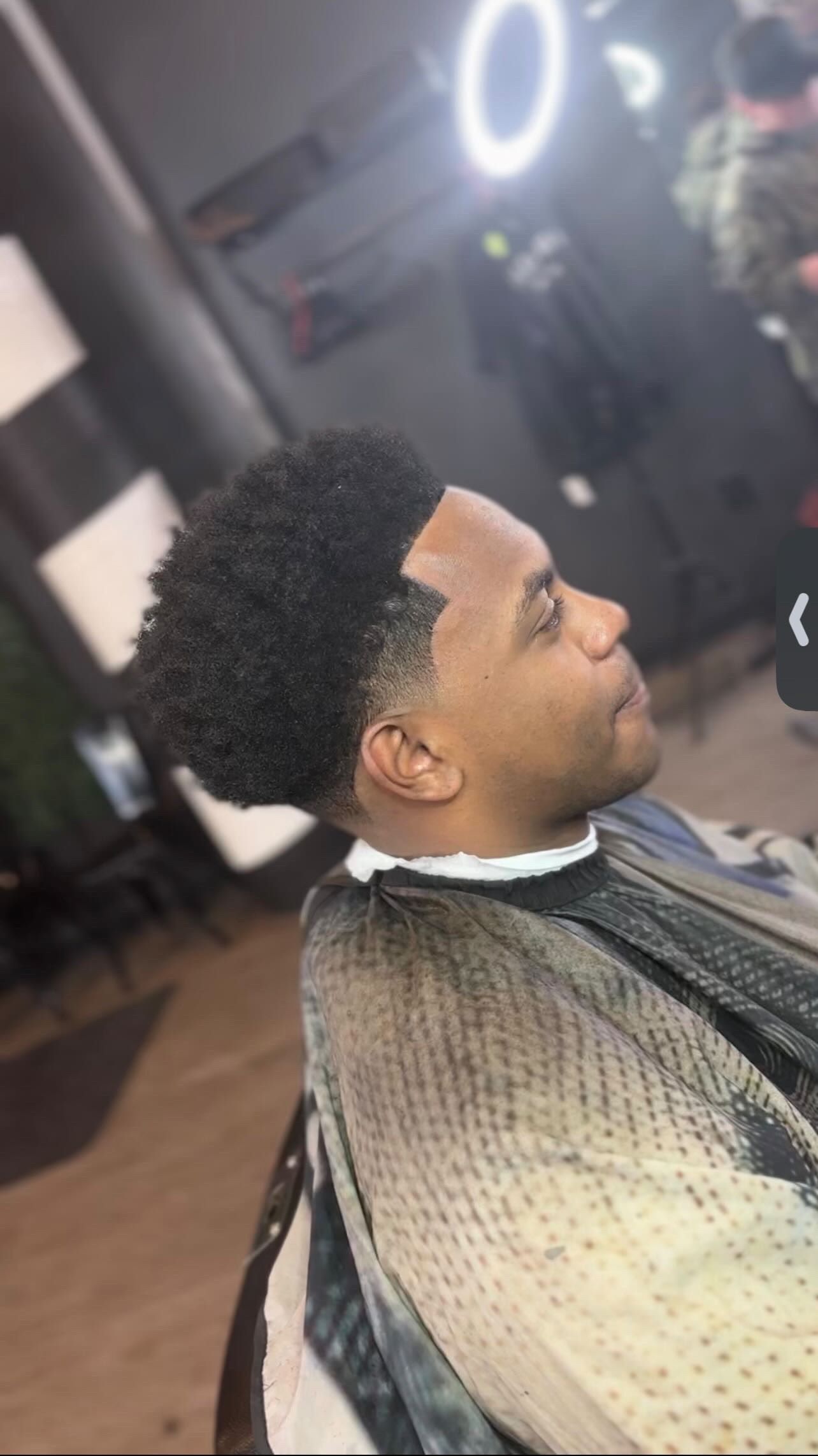 Man in a barber chair with a fresh haircut. Black hair with a skin fade, in a barbershop setting.