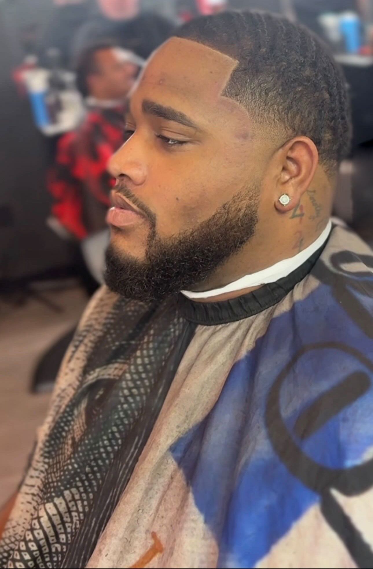 Man with neat haircut, beard, wearing a patterned barber cape, in a salon.