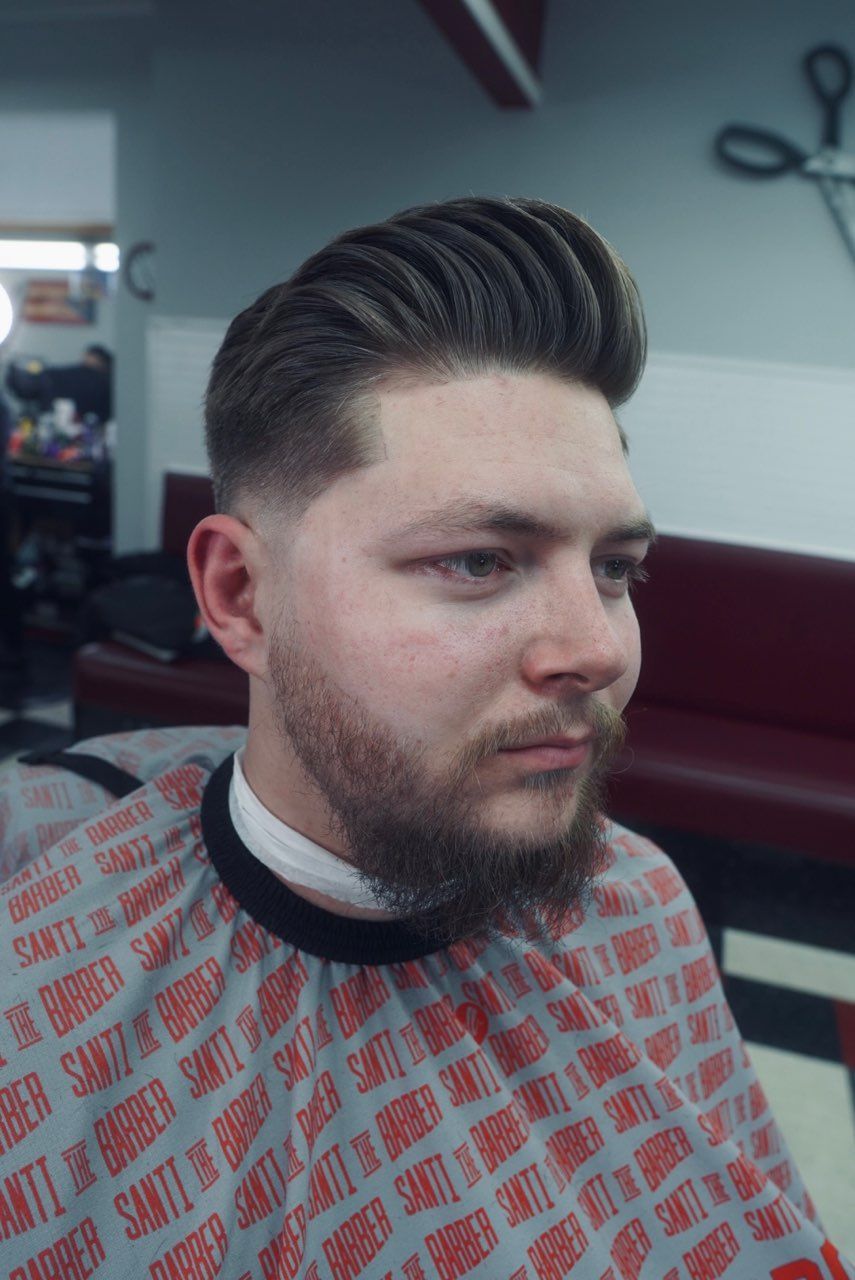 A man with a beard is getting his hair cut at a barber shop.