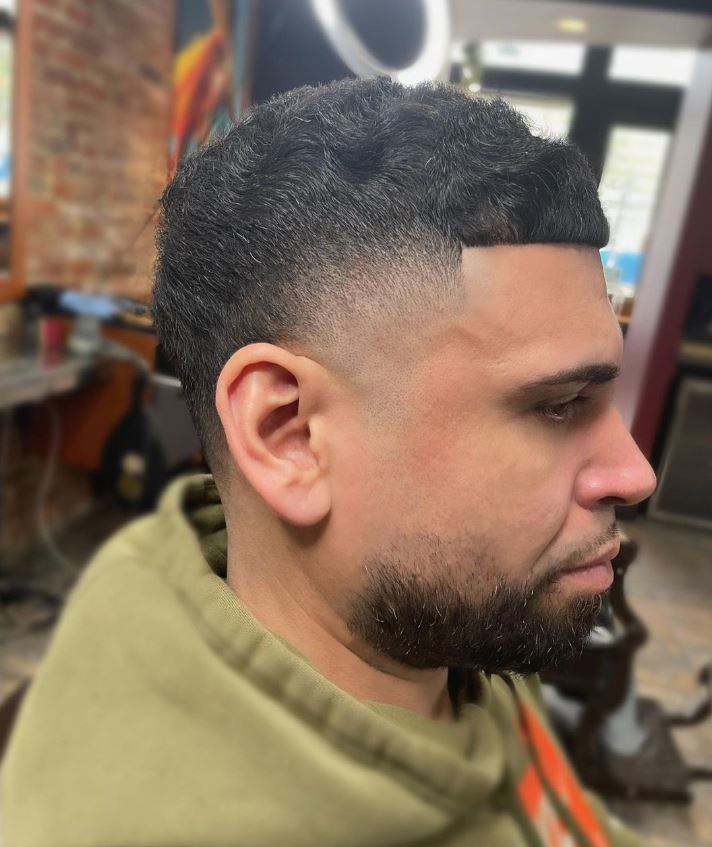 A man with a beard is getting his hair cut at a barber shop.