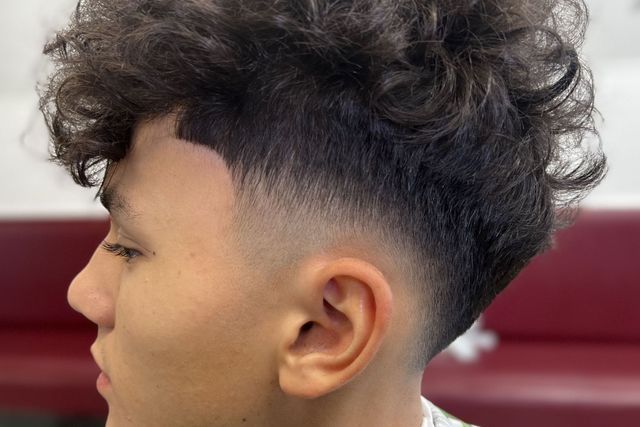 A young man with curly hair is getting his hair cut at a barber shop.