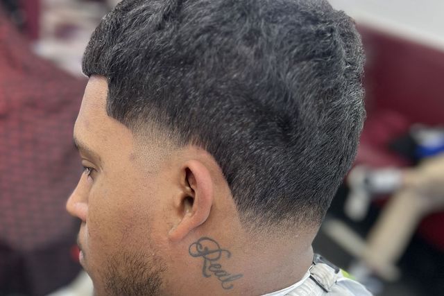 A man with a tattoo on his neck is getting his hair cut at a barber shop.