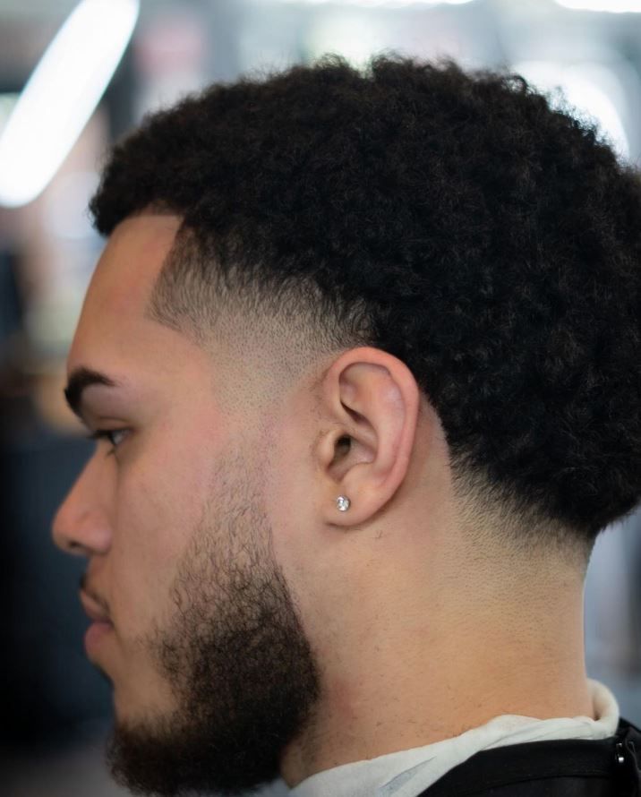 A man with curly hair and a beard has earrings in his ears