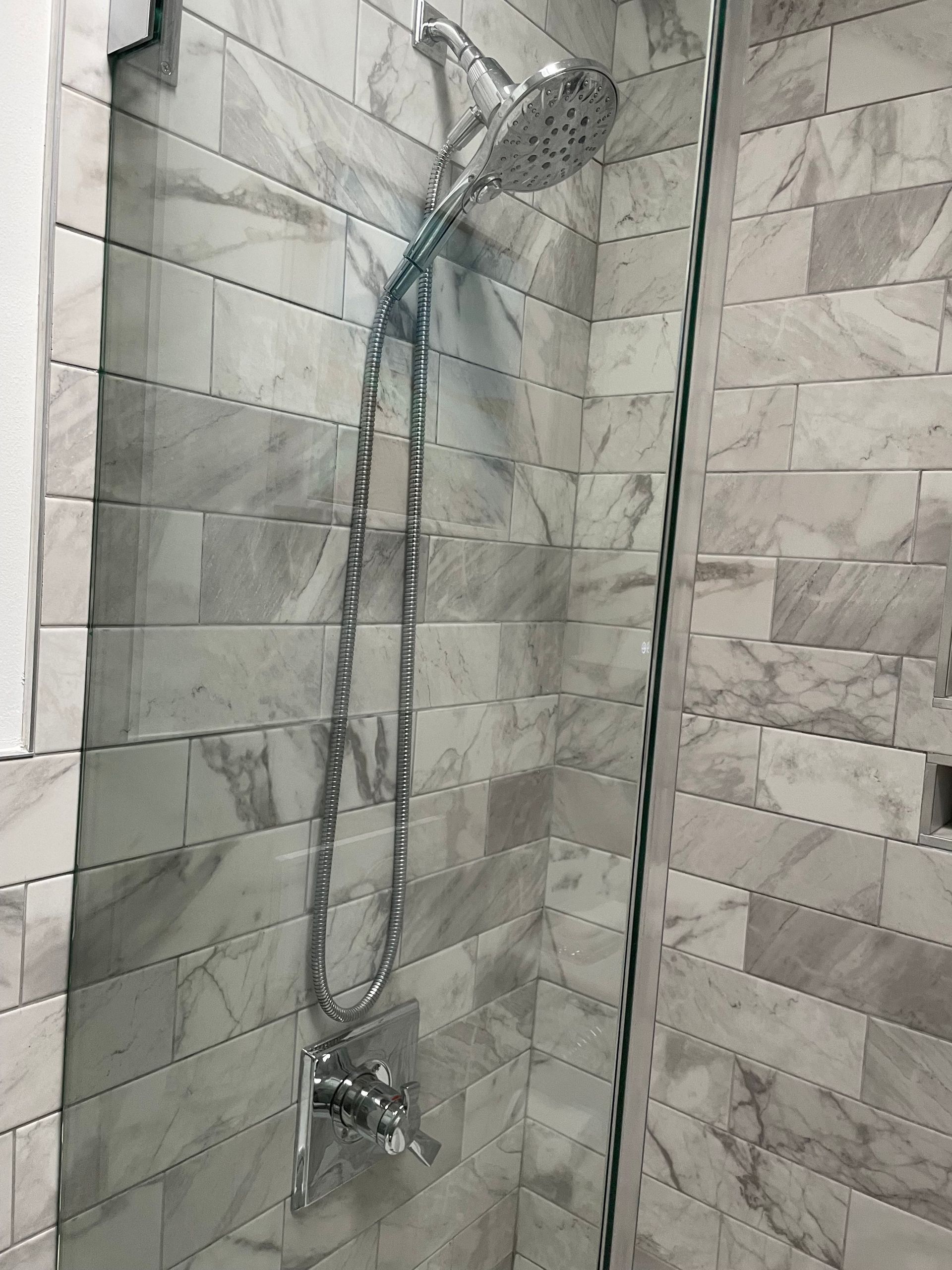 Chrome showerhead and handheld shower in a tiled bathroom shower stall