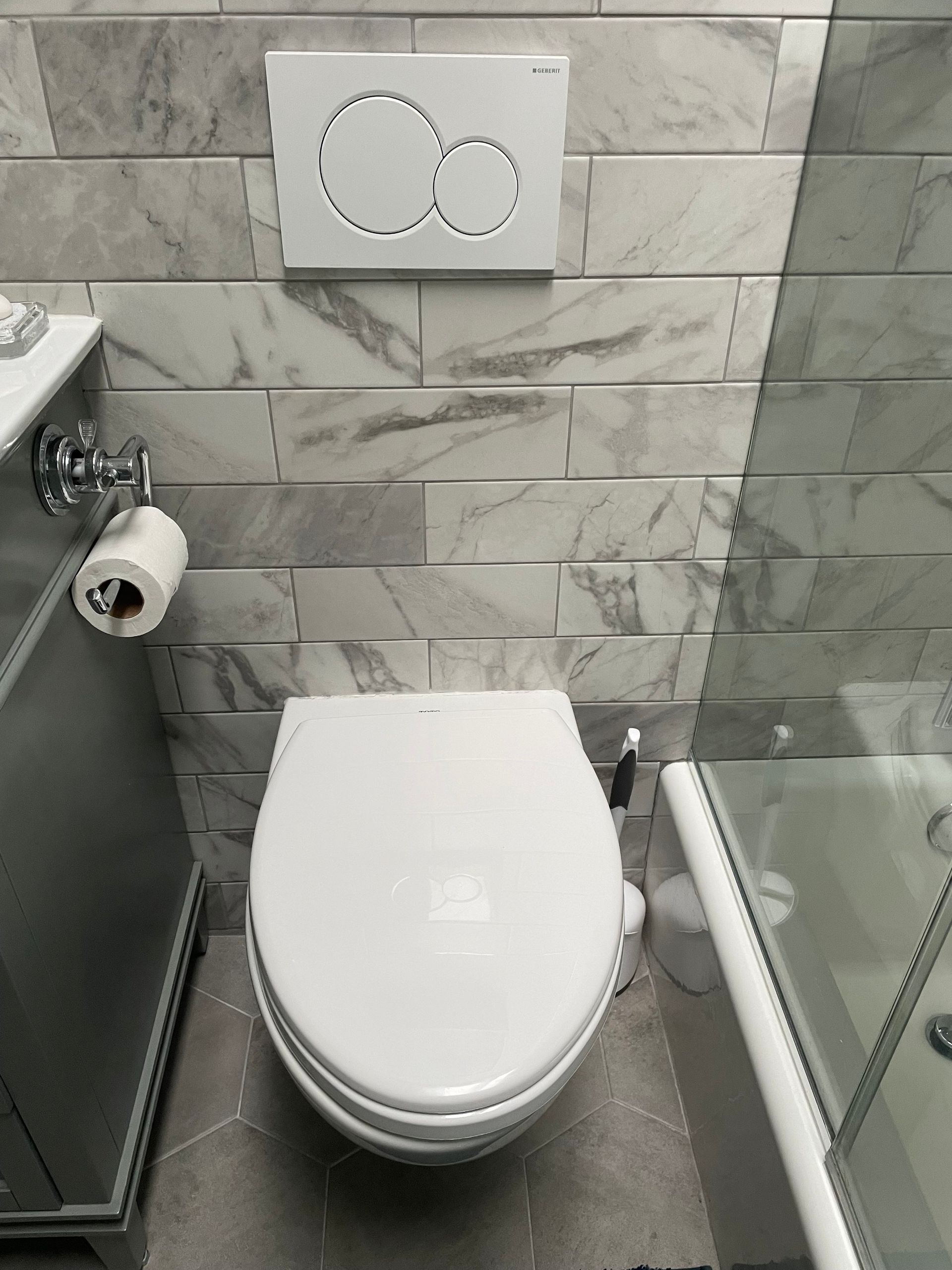Small modern bathroom with a wall-mounted toilet, gray tile walls, and a glass shower partition.