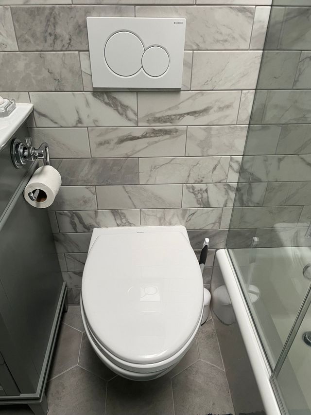 Small bathroom with a wall-mounted toilet, gray tile walls, and a glass shower partition.