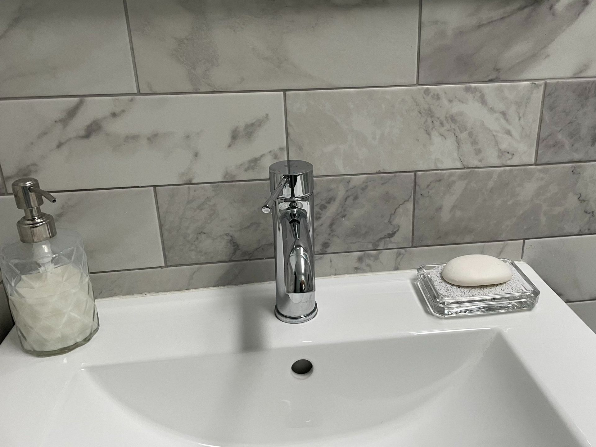Bathroom sink with chrome faucet, marble tile backsplash, soap dish, and bar soap.