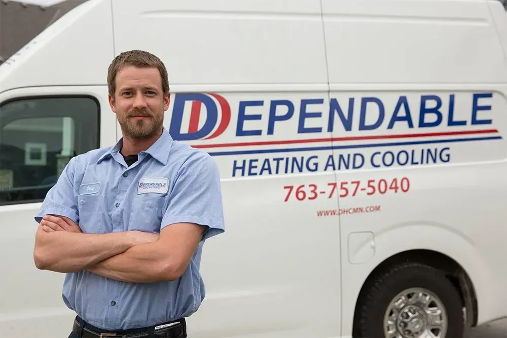 HVAC technician in blue shirt with arms crossed, next to a white van with 