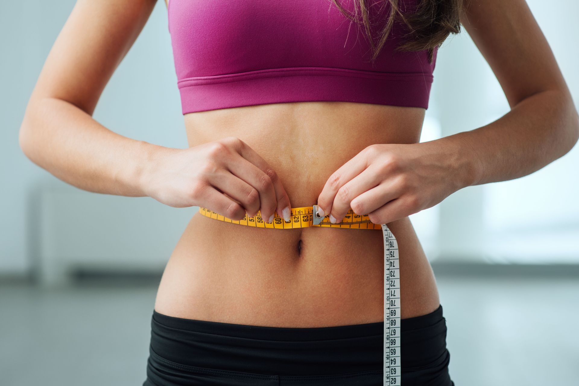 A woman is measuring her waist with a tape measure.