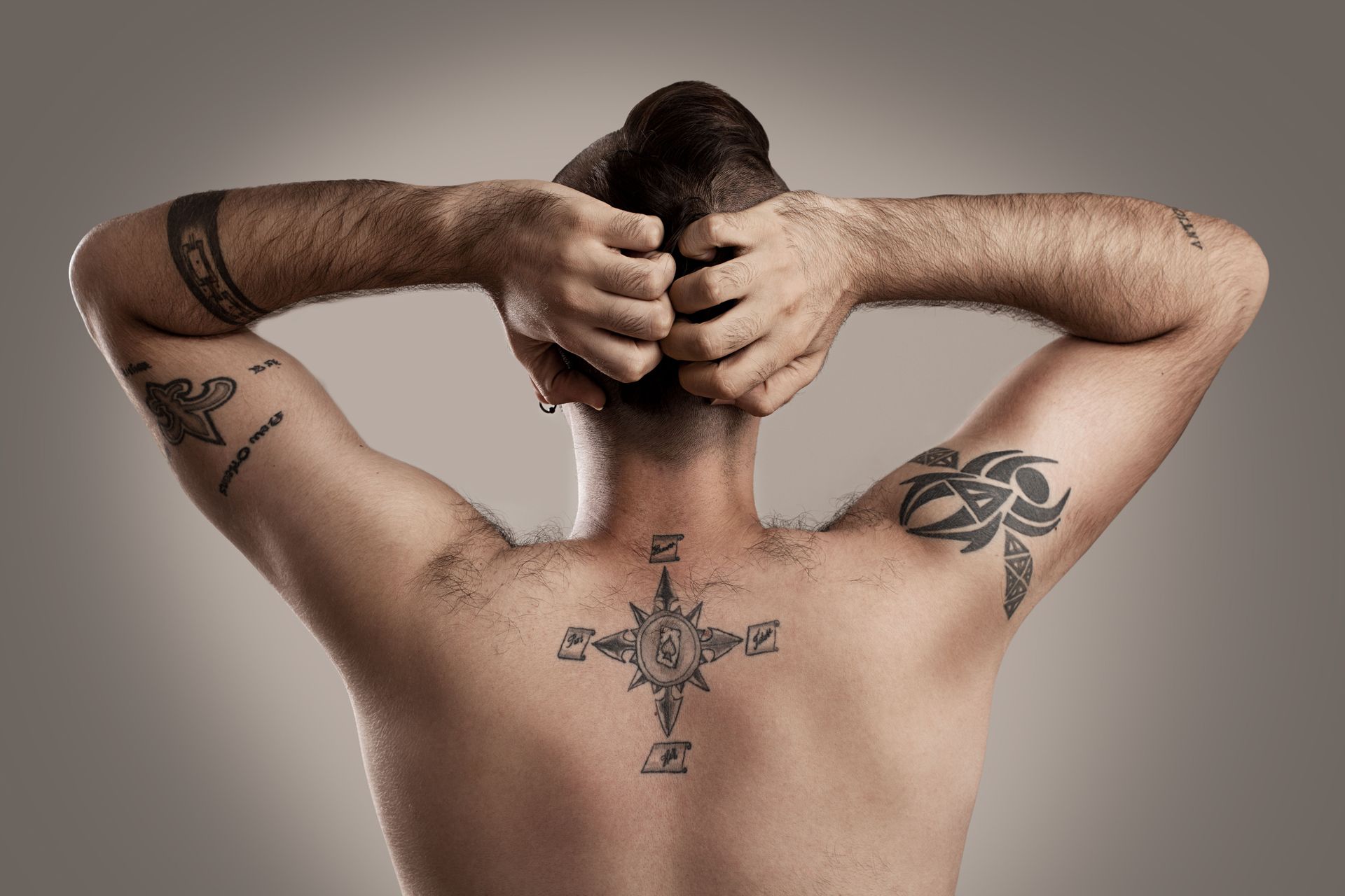 A man with a tattoo on his back is holding his hair in a bun.