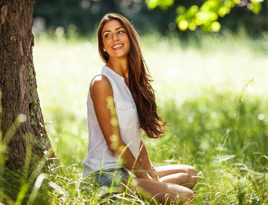 A woman is sitting under a tree in the grass.