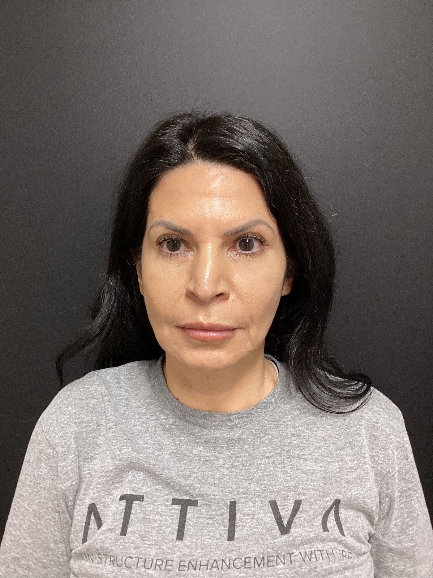 Woman with dark hair in a gray sweatshirt, facing the camera. Dark background.