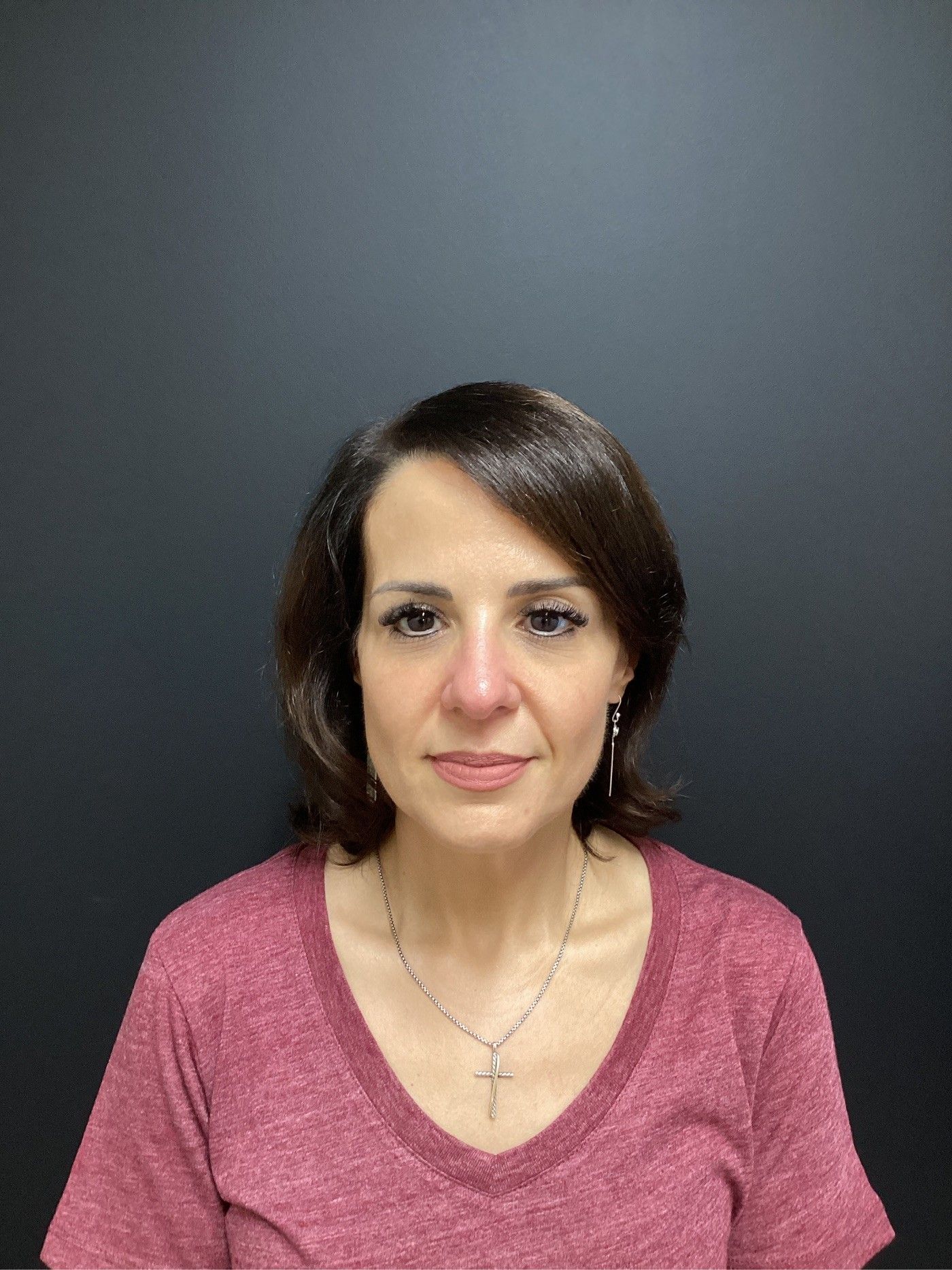 Woman with dark hair and a maroon shirt, wearing a cross necklace, against a black backdrop.