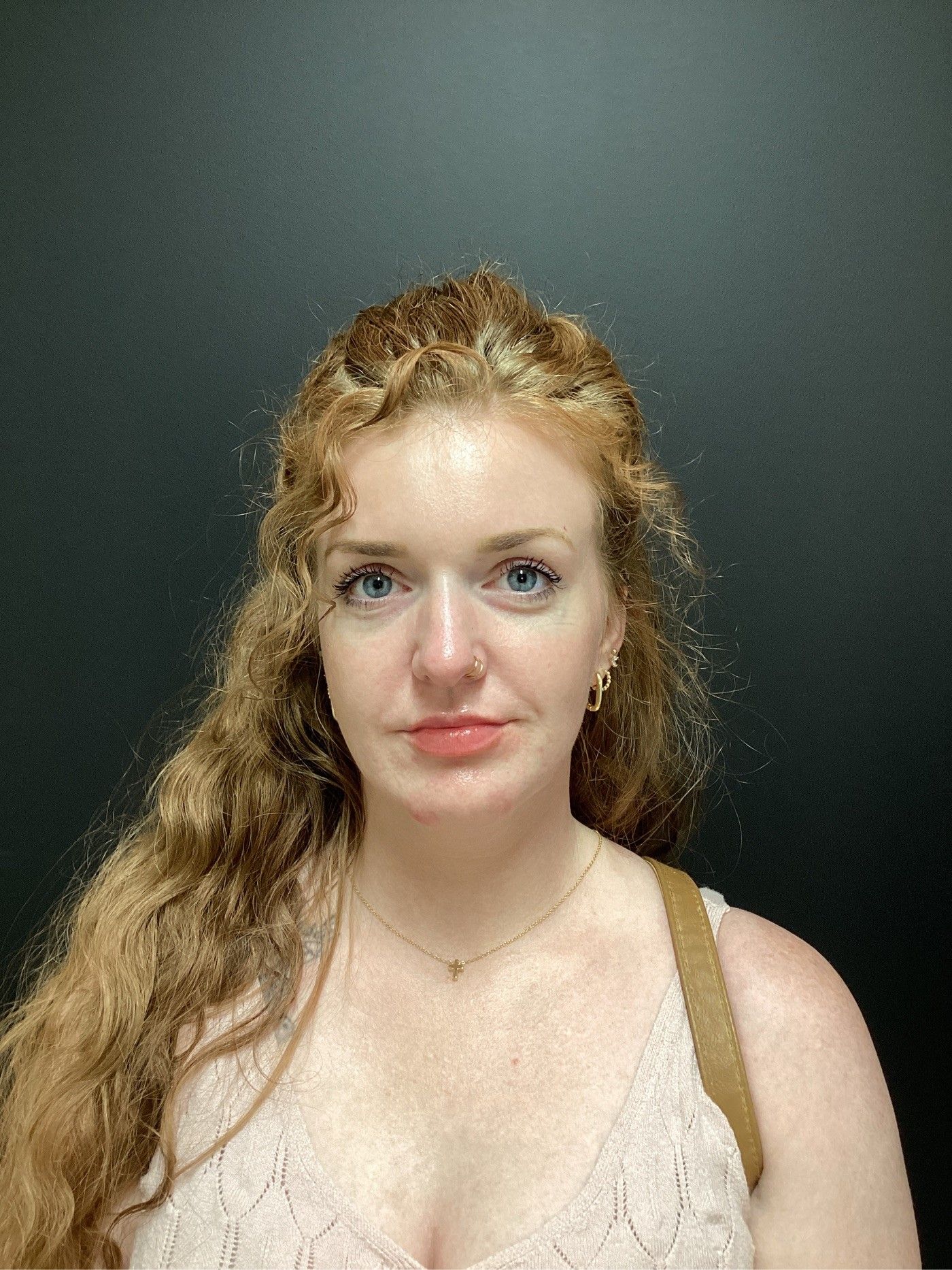 Woman with curly red hair, pale pink top, looking at the camera with blue eyes. Dark background.