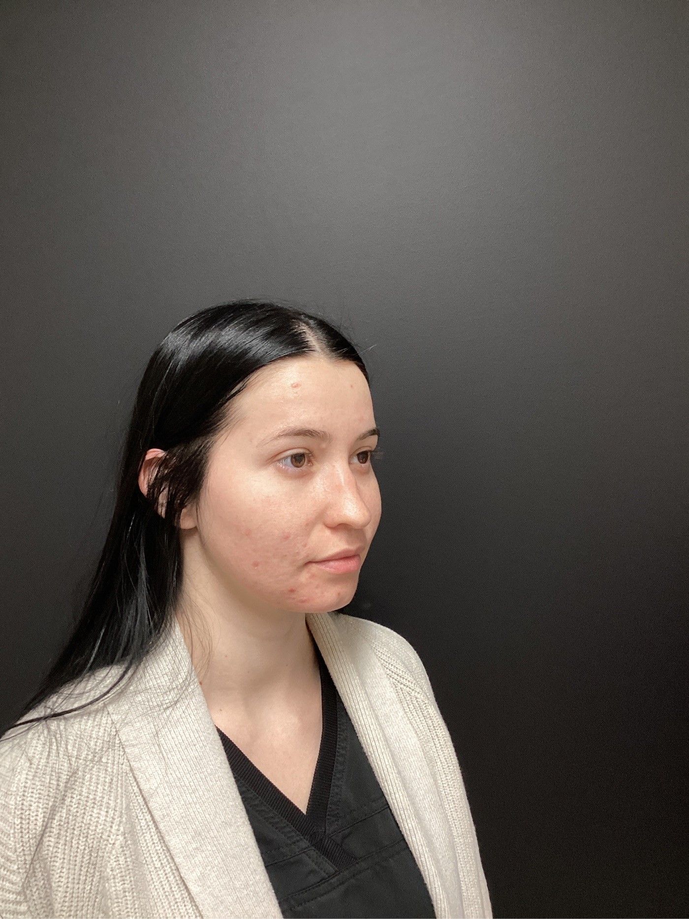 Woman with dark hair in profile, wearing a light cardigan over a dark top, against a dark background.