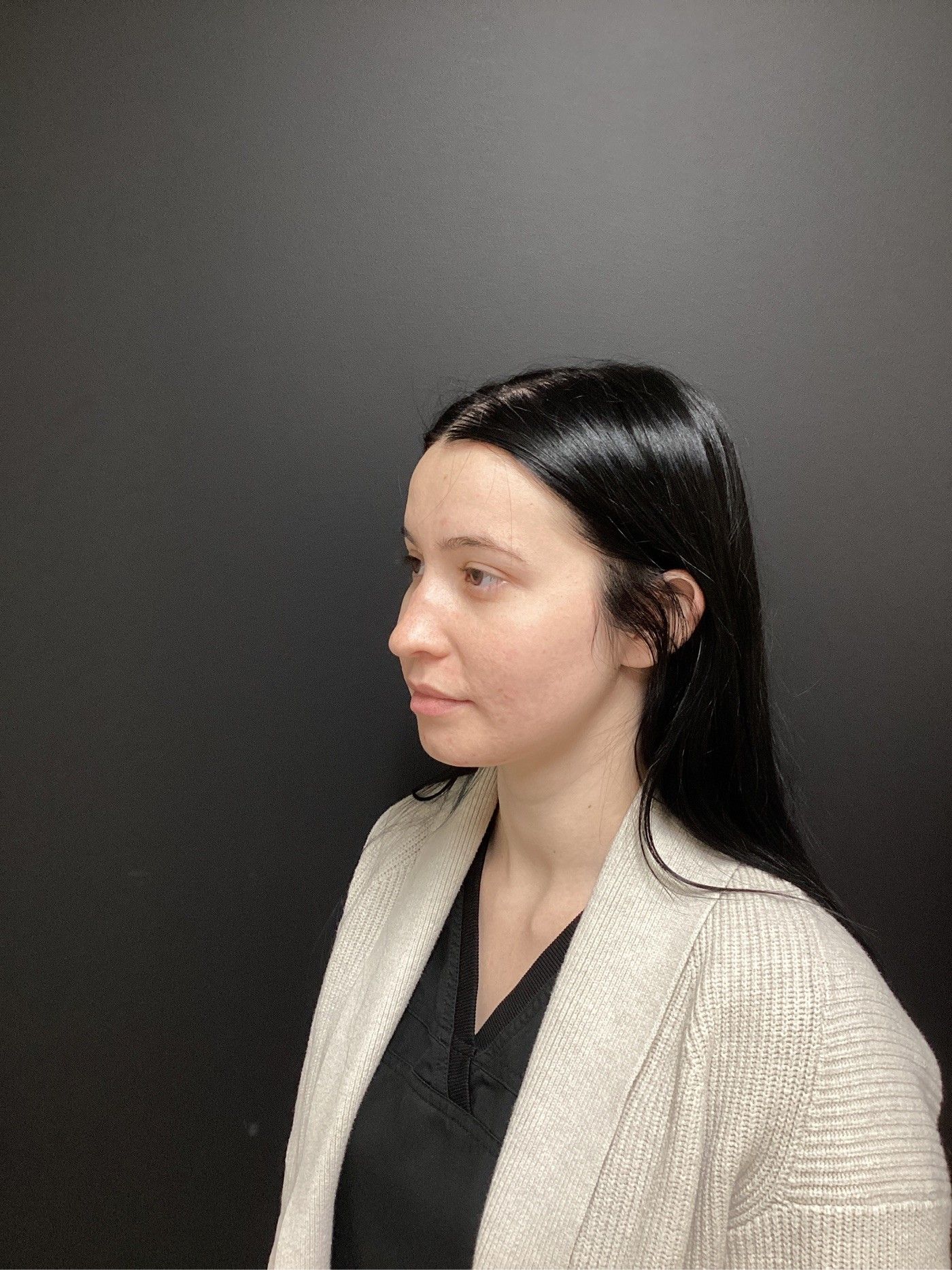 Woman in light blazer against a dark wall, looking to the side.