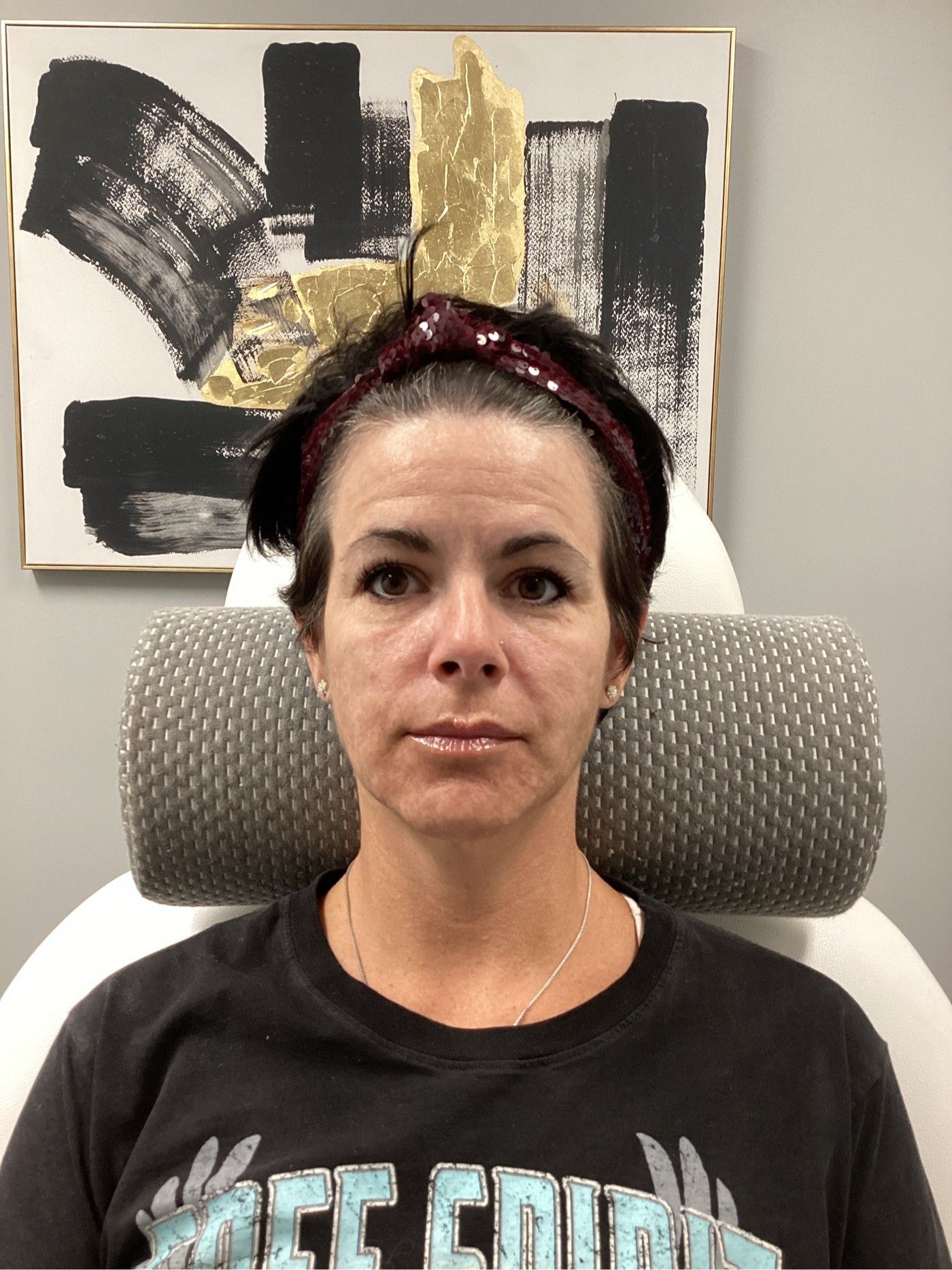 Woman seated in chair; neutral expression, wearing a headband and dark t-shirt. Background: abstract art.