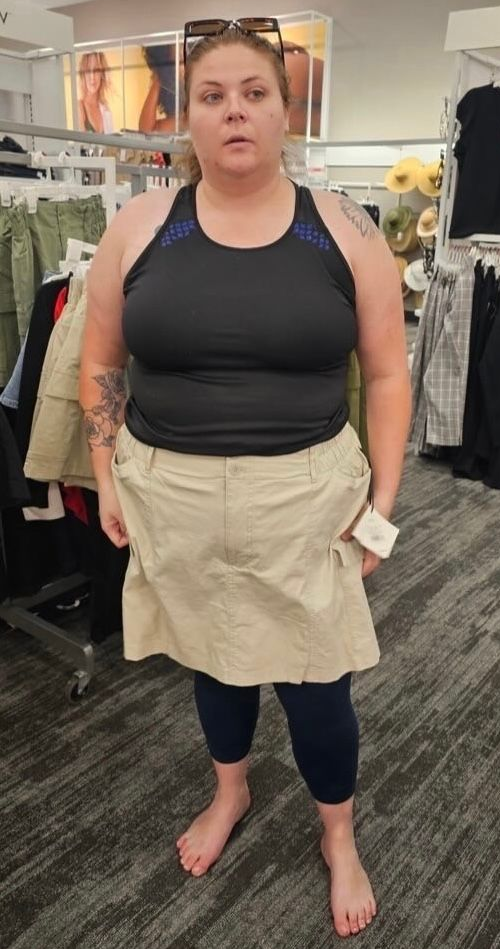 Woman in black top, khaki skirt, and leggings in a clothing store, barefoot.