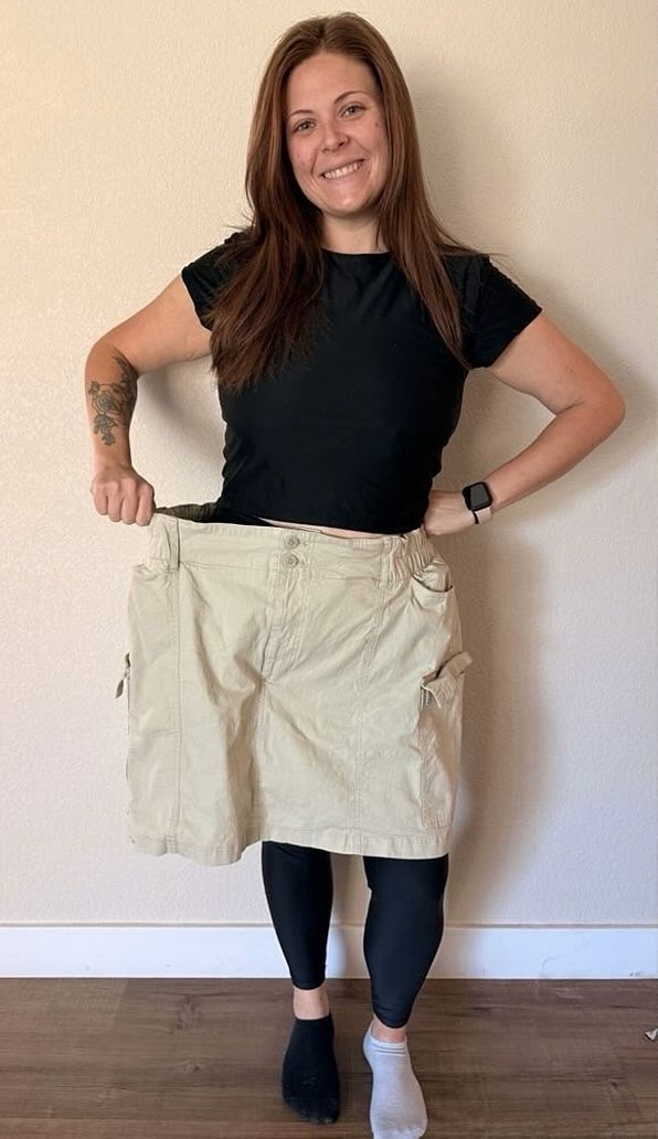 Woman holds oversized khaki shorts, smiling, showing weight loss success.