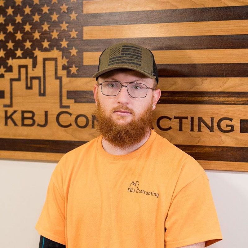 A man with a beard and glasses is standing in front of a kbj construction sign