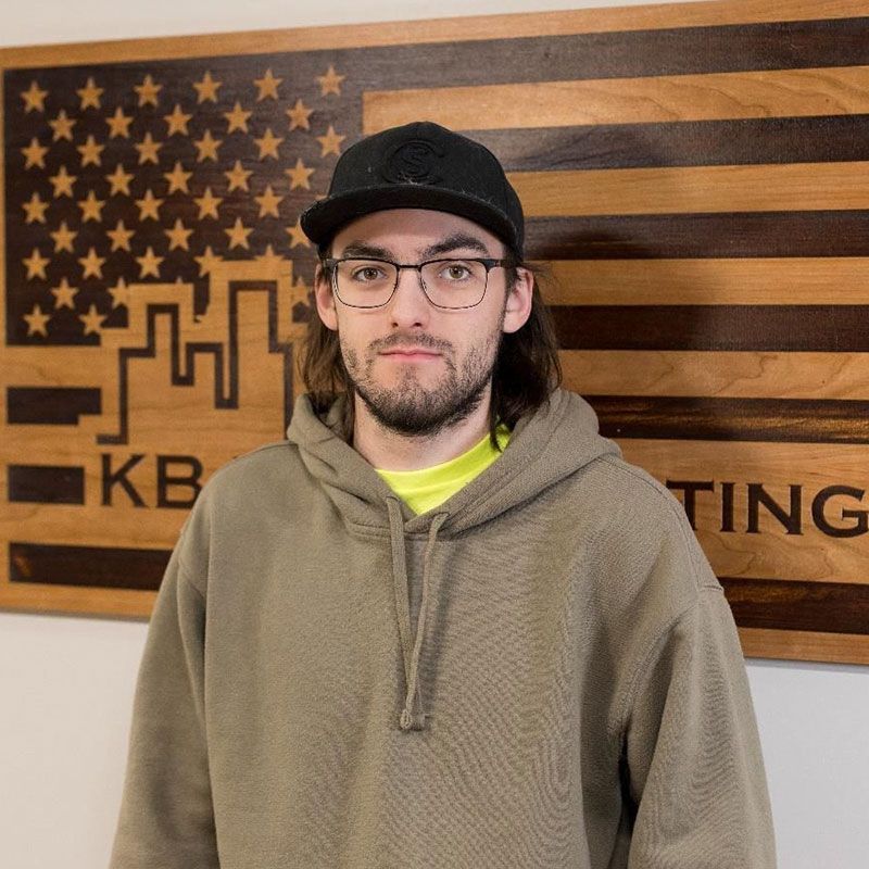 A man wearing glasses and a hat is standing in front of an american flag