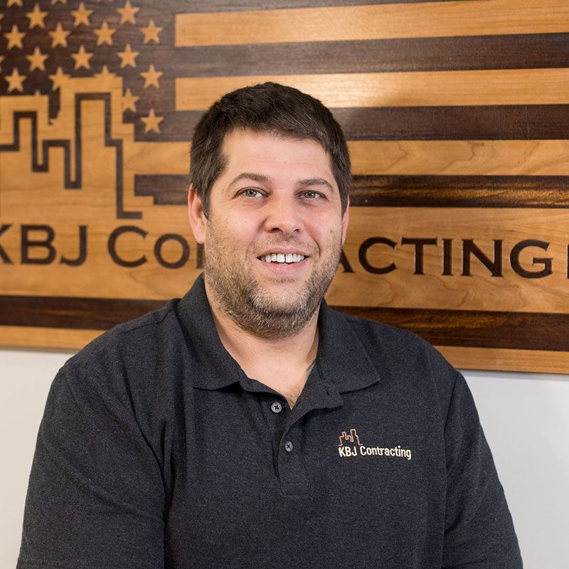 A man is smiling in front of a sign that says kbj construction